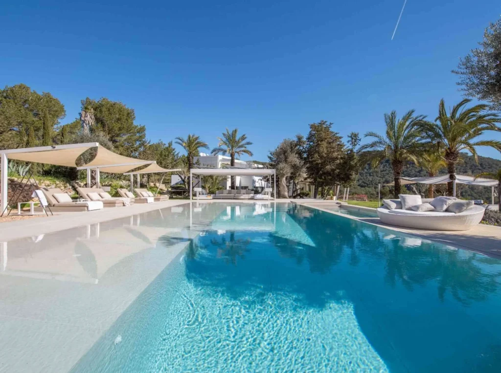 Luxury villas in ibiza, a large swimming pool surrounded by a spacious luxury villa, showcasing elegant architecture and lush landscaping.
