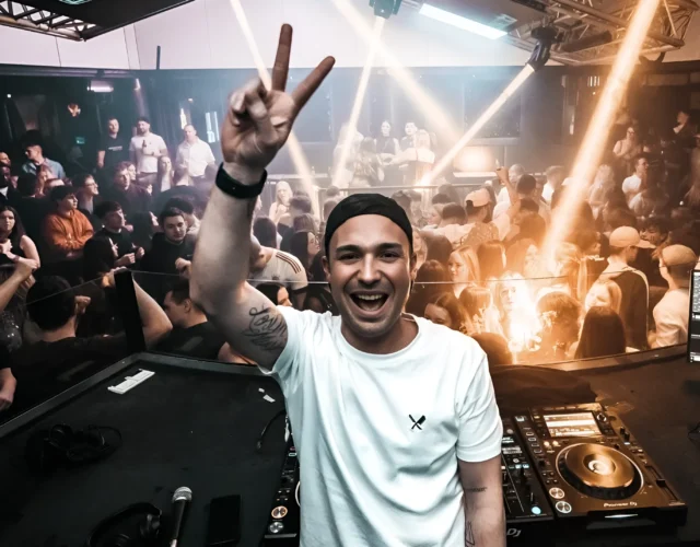 A DJ with hands raised, energizing a large audience during an electrifying performance.